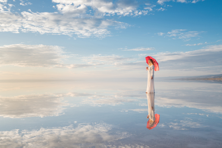 A woman in white seems to stand on the surface of a lake.