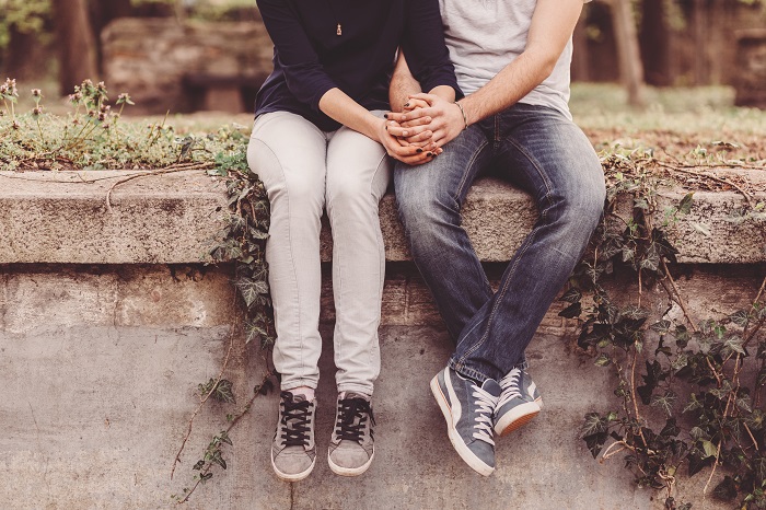 Lower half view of a couple sitting on a concrete ledge next to a forest