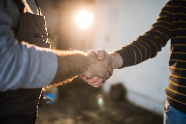 Two men shake hands while a work lamp shines in the background