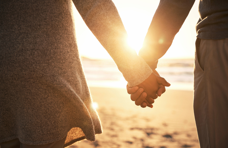A couple holds hands on the beach.