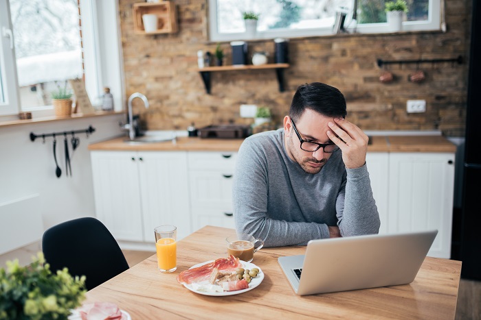 Hypochondriac sitting at breakfast table looking up symptoms on his computer.