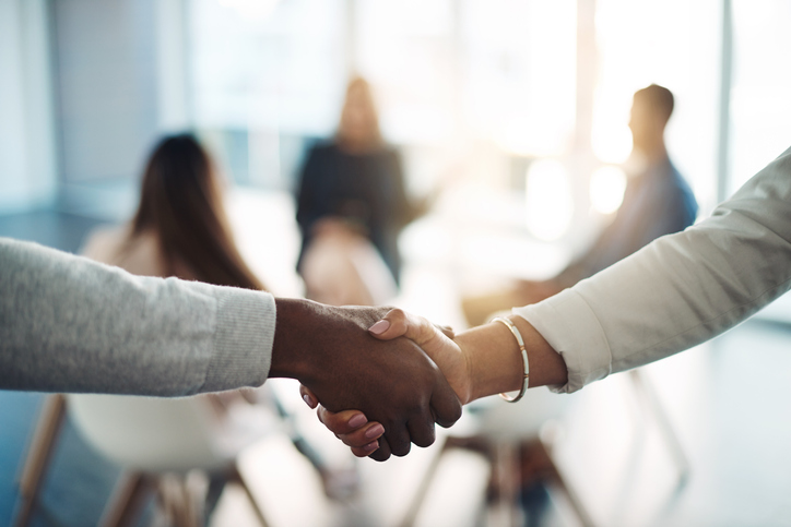 Coworkers shake hands in sunlit office.