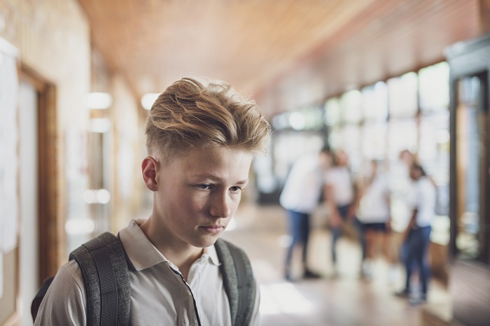 Boy at school, downcast, while a group of friends stands in the background