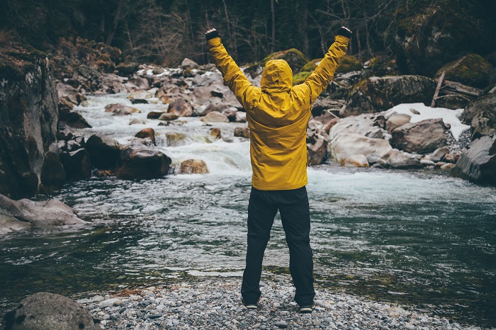 Man standing in river watching waterfall, hands up in victory