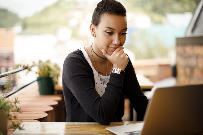 College student sits in a cafe, reading something on their laptop