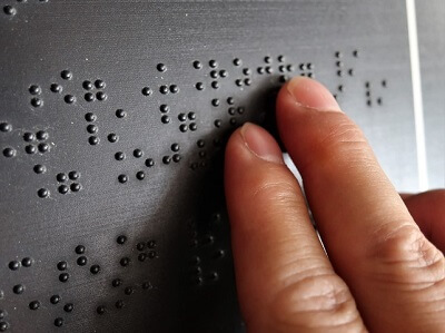 Close-up of fingers reading braille sign.