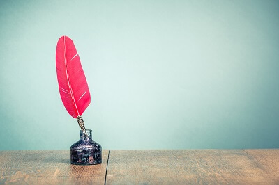 Red feather quill in ink pot with aqua background