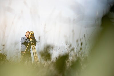 View of surveyor working in field through blades of grass