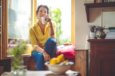 Woman sitting in her kitchen with a cup of coffee, reflecting on forgiveness