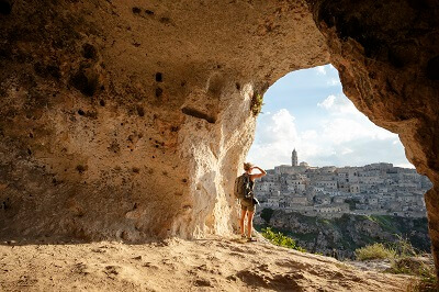 Solo traveler standing in cave, looking out onto an old city