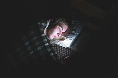 Teen boy perusing the internet on his phone in bed at night