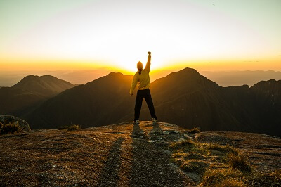 Man standing on top of mountain at sunrise, one hand raised in victory