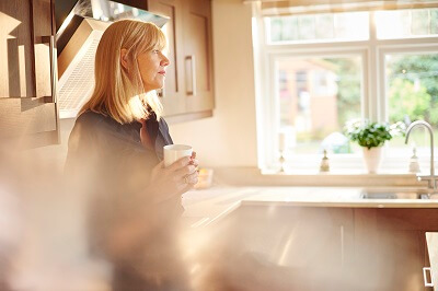 Woman standing in kitchen drinking coffee, looking contemplative 