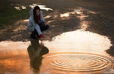 Woman crouching by puddle, admiring her reflection