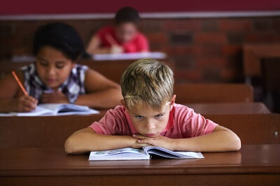 Boy at his desk with his head resting on his hands, looking angry