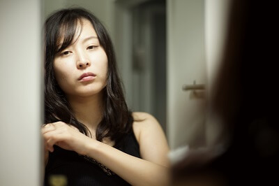 Woman looking at her reflection in the mirror with self-criticism