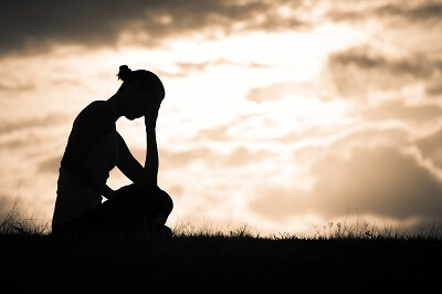 Silhouette of woman sitting in a field, her head in her hands