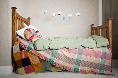 Bed with colorful blankets next to wall with sheep jumping over fence