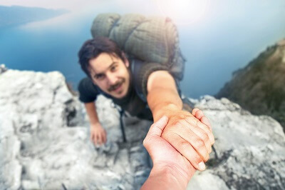 Man being helped up difficult spot by friend while rock climbing