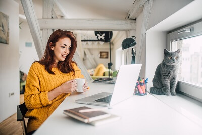 Woman working on her computer with a cat sitting nearby