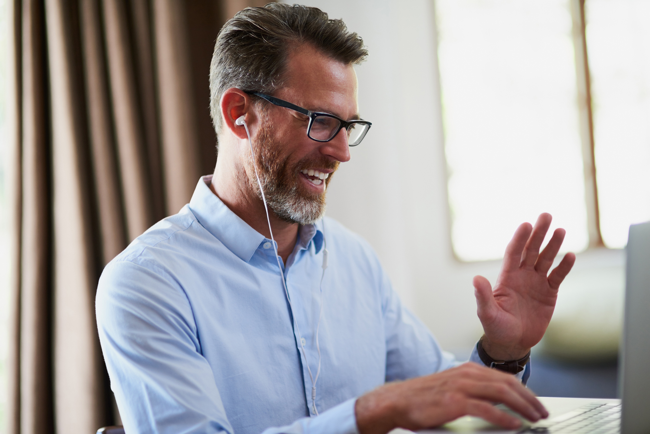 Male therapist waving at colleague over video conference.