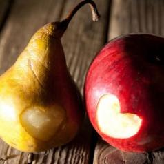 An apple and a pear have a the shape of an heart carved into the skin.