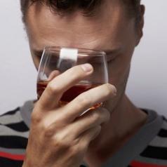 Stressed man presses glass of liquor to his forehead