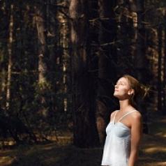 A young woman in woods looks up.