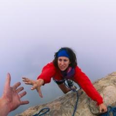 A woman reaches for a helping-hand as she climbs a rock.