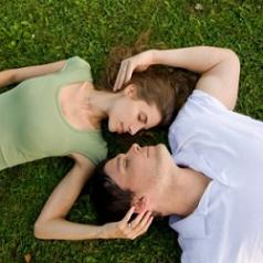 Couple lying face-to-face outside, with eyes closed