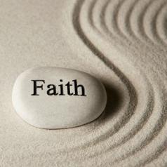 A rock that says "faith" on it sits in sand that has been raked into a wavy design.
