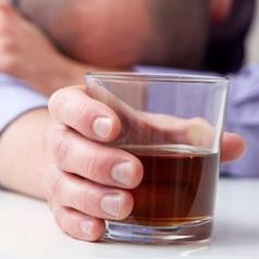 A man clasping a glass of liquor rests his head on his arm