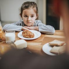 Young girl looks unhappy as she sits at the table with her parent at breakfast