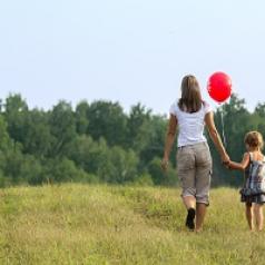 Mother and daughter walking in field with red balloon