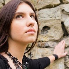 Young woman looks towards sky while leaning on stone wall
