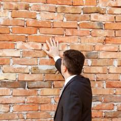 Man in a suit touching a brick wall