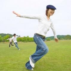 Three young adults run around a grassy field with their arms out.