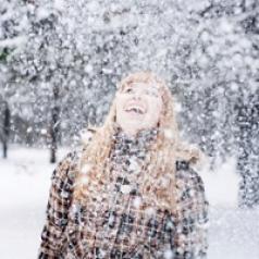 A woman happily plays in the snow alone.