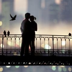 Couple standing on bridge with city lights in background