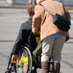 A woman pushes her husband in a wheel-chair.