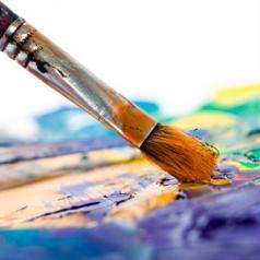 A close-up picture of a paint brush dipping into a palette of mixed pain colors.
