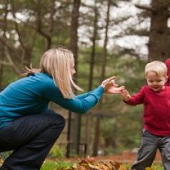 Parents help their infant walk in a forested setting