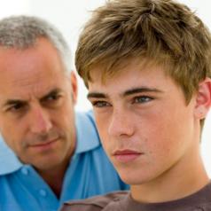 A teen looks into the distance as his father watches him