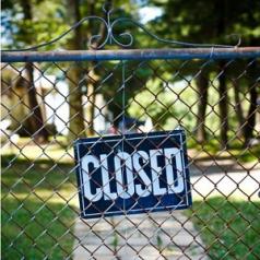 A wire fence is shut and has a closed sign on it.