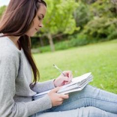 Girl sits in grass writing in a journal