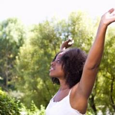 Woman standing in sun with arms raised up