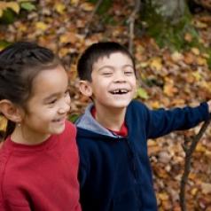 Two kids laugh while hiking through woods