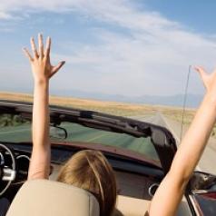 woman riding in convertible with arms raised