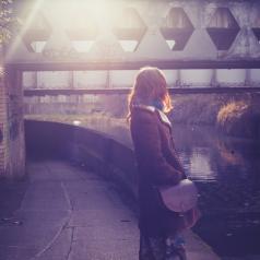 Rear view of person with long hair, head turned away, standing by canal at sunset