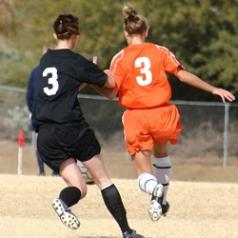 Two female soccer players from opposing teams vie for the ball